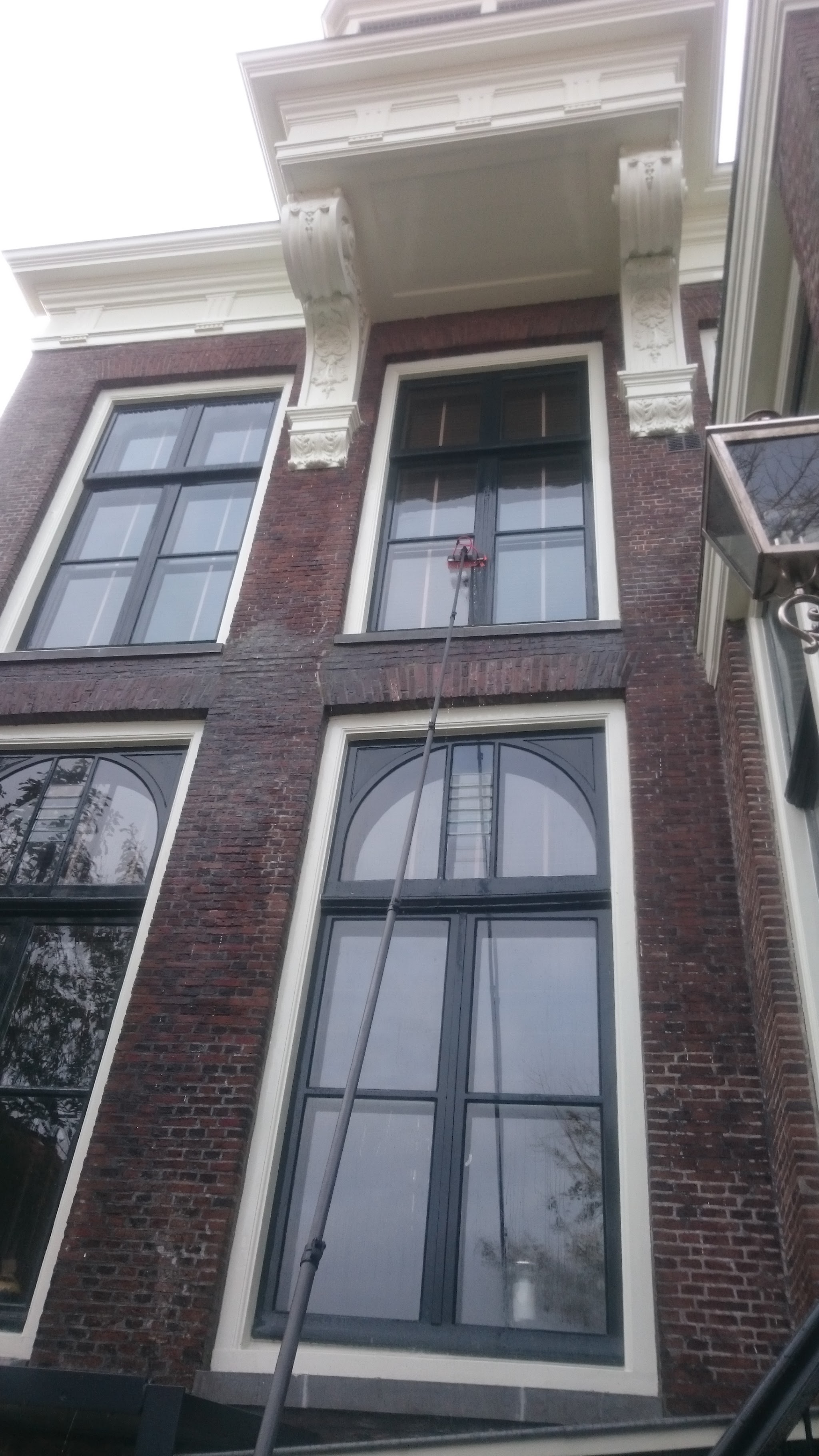 Hoge gevel van een historisch pand met sierlijsten, de telescoopsteel reikt tot het bovenste raam